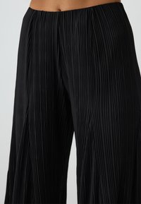 Pantalons larges plissés noirs en tissu léger, avec un design texturé, une taille élastique et une silhouette fluide.