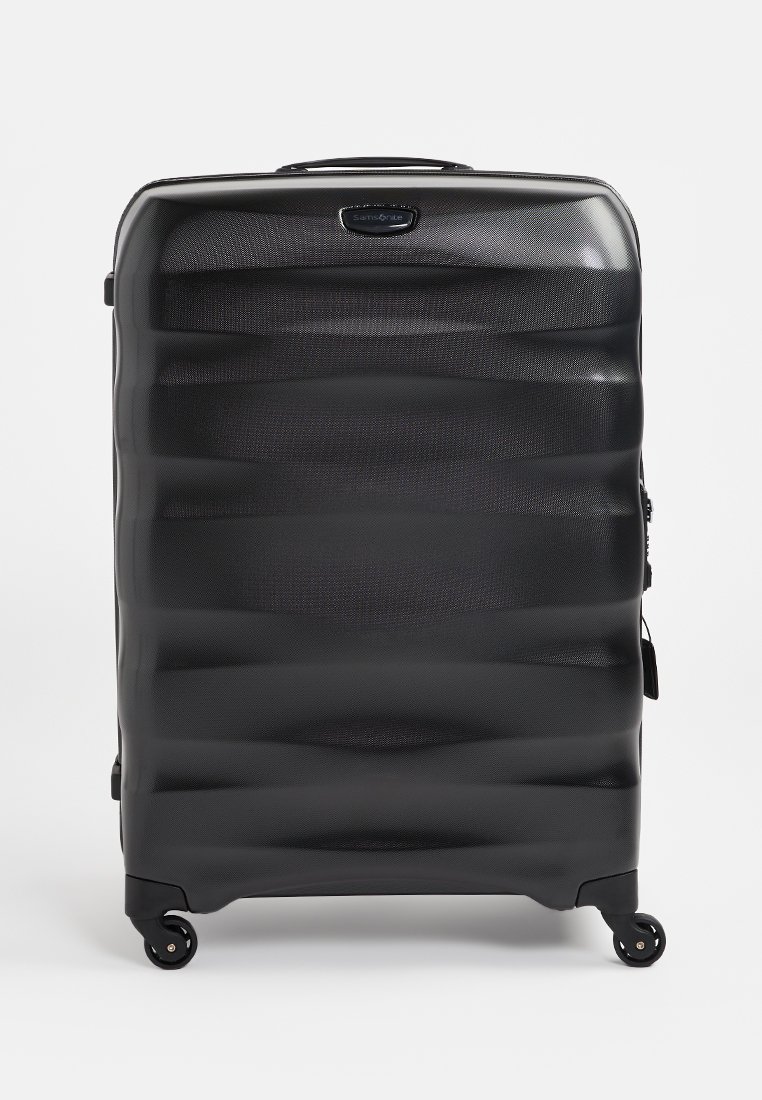 Schwarzer Hartschalenkoffer mit strukturierter Oberfläche, wellenförmigem Design und vier Rädern. Verfügt über einen oberen Griff und einen Reißverschluss.