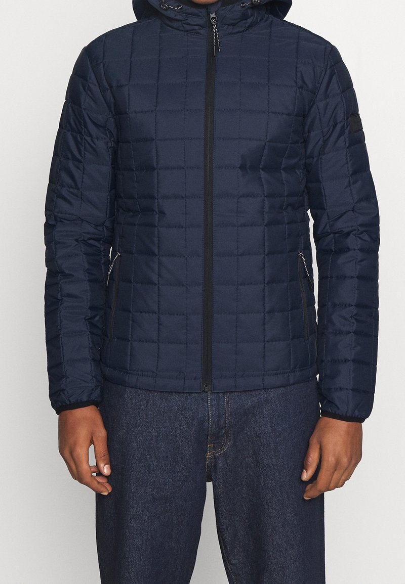 Navyblauwe gearceerde jas met capuchon, voorzien van een volledige rits en zijzakken. Het materiaal heeft een gladde textuur en is licht van gewicht.
