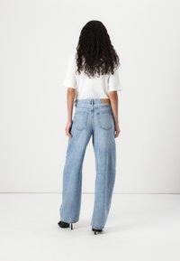 Lys blå høy midje vide ben jeans med en falmet vask, to baklommer og et lærpatch på livlinjen.