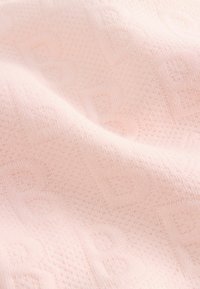 Vaaleanpunaista teksturoitua kangasta, jossa on hienovarainen kohotettu kuvio. Pehmeä materiaali laskeutuu lempeästi, ja se osoittaa hienoa neulosta, jossa on tasaista ommelta.