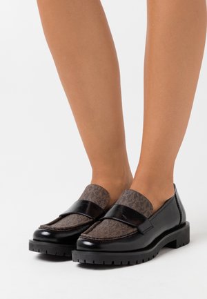 Mocassins en cuir noir avec un dessus en cuir texturé brun et des accents noirs. Semelle en caoutchouc épaisse, bout arrondi et surpiqûres décoratives.