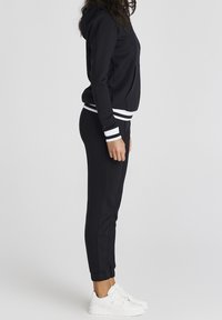 Černá mikina a odpovídající tepláky s bílými pruhy na manžetách a v pase. Obsahuje přední kapsu a ribbed texturu. Nosit s bílými teniskami.