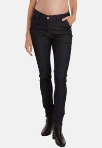 Jean en denim bleu foncé avec coupe slim, taille mi-haute, design à cinq poches et couture dorée. Équipé d'une fermeture à bouton et à zip à l'avant.