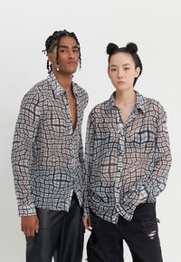 To personer iført gennemskinnelige, mønstrede skjorter med et ternet design i brun, blå og hvid. Skjorterne har knaplukninger og lange ærmer.