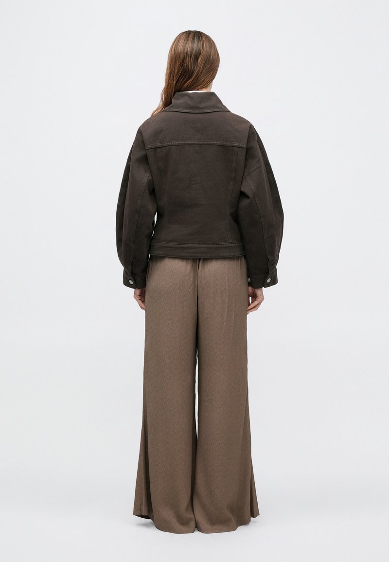 Veste en denim marron avec un large col, des épaules tombantes et une coupe décontractée, associée à un pantalon beige taille haute à jambes larges.