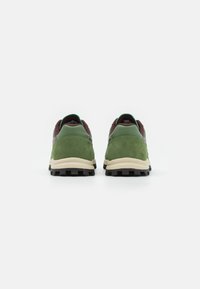 Paar grüne Wildleder- und Leder-Sneaker mit beigen Zwischensohlen und schwarzen Profilsohlen, von hinten auf einem weißen Hintergrund betrachtet.
