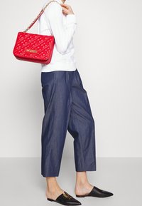 Röd quiltad handväska med guldfärgade detaljer, bärs på axeln. Matchad med mörkblå byxor med lös passform och svarta slip-on skor.