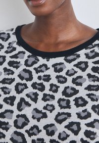 Sweatshirt cinza com padrão de onça preto, apresentando um decote canelado preto. Textura suave, vista aproximada do tecido.