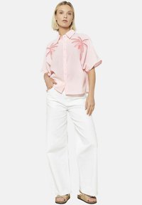 Camicia a maniche corte rosa con righe, ricamo di palme, chiusura con bottoni e vestibilità rilassata, abbinata a pantaloni bianchi larghi e sandali.