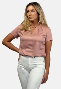 Short-sleeve pink blouse with a V-neck and pleated detail, made from smooth fabric; worn with white fitted jeans.