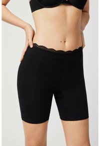 Pantalones cortos de algodón negros con una cinturilla de encaje con volantes y una silueta ajustada, que presentan una textura suave y un corte a la altura de la rodilla.