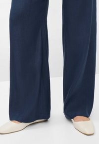 Pantaloni a gamba larga di colore blu navy realizzati in un tessuto leggero, abbinati a ballerine a punta di colore crema. Design semplice, senza motivi visibili.