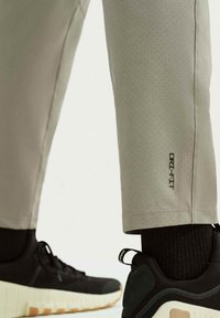 Αθλητικό παντελόνι ανοιχτό γκρι Dri-FIT με διάτρητη υφή και μαύρη λεπτομέρεια λογότυπου, σε συνδυασμό με μαύρα παπούτσια που έχουν χοντρή λευκή σόλα.