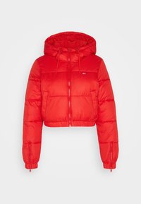 Giacca a vento rossa corta con cappuccio, cerniera frontale e coulisse. Presenta polsini elasticizzati e una toppa con logo sul petto. Texture liscia.