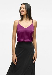 Violetsatinė camisole su plonomis spaghetti petnešėlėmis ir V formos iškirpte, derinama su plačiais juodais sijonais. Lygus paviršius; lengvas dizainas.