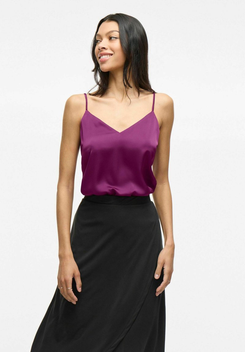 Violetsatinė camisole su plonomis spaghetti petnešėlėmis ir V formos iškirpte, derinama su plačiais juodais sijonais. Lygus paviršius; lengvas dizainas.