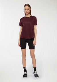 Bordowa koszulka sportowa z krótkim rękawem, w połączeniu z czarnymi szortami rowerowymi. Zawiera wzorzyste czarno-białe skarpetki oraz czarne buty sportowe.