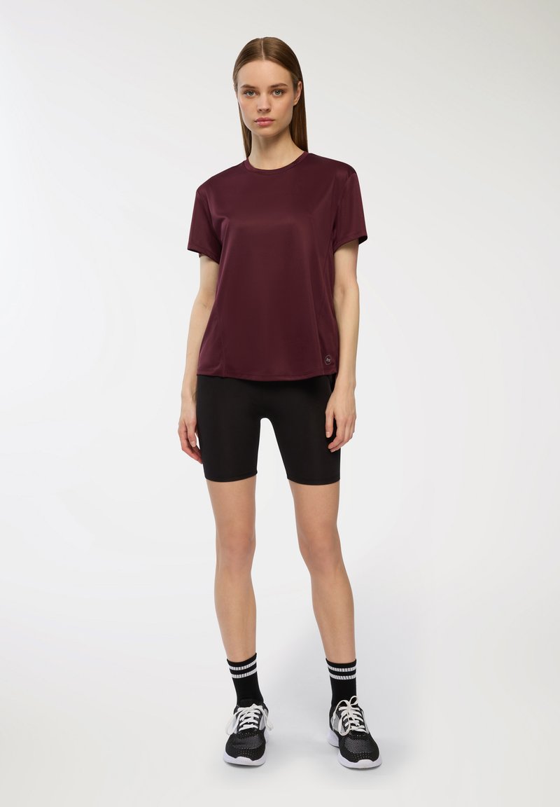 Bordowa koszulka sportowa z krótkim rękawem, w połączeniu z czarnymi szortami rowerowymi. Zawiera wzorzyste czarno-białe skarpetki oraz czarne buty sportowe.