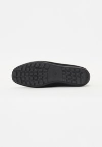 Semelle de chaussure noire en caoutchouc texturé pour une meilleure adhérence, avec un motif en grille et des bords lisses. Design léger avec un dessus en maille respirante.