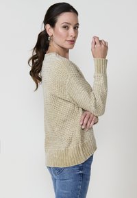 Beez värvi kudum, millel on tekstuuritud disain, soonikkoes varrukad ja äär. Koos siniste teksadega, on see lõdva lõikega ja kergete külgsislitustega.