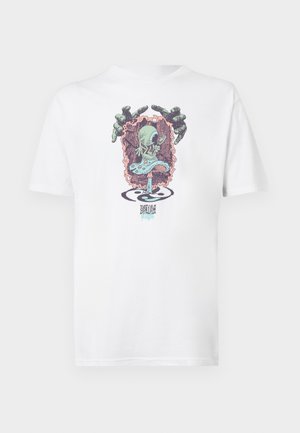 T-shirt en coton blanc avec un graphique coloré représentant un alien dansant et des mains sur un fond rose, agrémenté de motifs tourbillonnants.