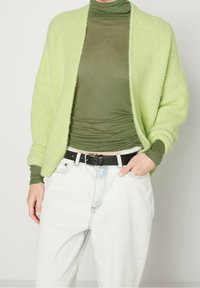 Cardigan verde chiaro in maglia con apertura frontale, tessuto strutturato, abbinato a un dolcevita verde scuro e jeans a vita alta in denim chiaro. Cintura nera inclusa.