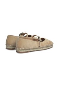 Espadrilles de ante en tono marrón con suela de yute trenzada. Presentan tiras cruzadas y un adorno metálico decorativo en la parte delantera. Diseño de puntera redondeada.