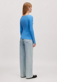 Blauwe langemouwen top met een ronde hals, gecombineerd met lichtgewassen wijde jeans en zwarte platte schoenen. Gladde textuur, fit ontwerp.