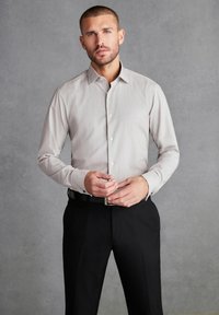 Jasnoszara, długosleeve koszula z subtelnym wzorem, z kołnierzykiem button-down i kontrastującymi czarnymi akcentami, zestawiona z ciemnymi spodniami i paskiem.