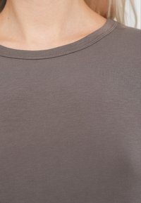 Material gri cu dungi și textură netedă, prevăzut cu un decolteu rotund. Vedere de aproape, concentrată pe detaliile materialului și ale culorii.