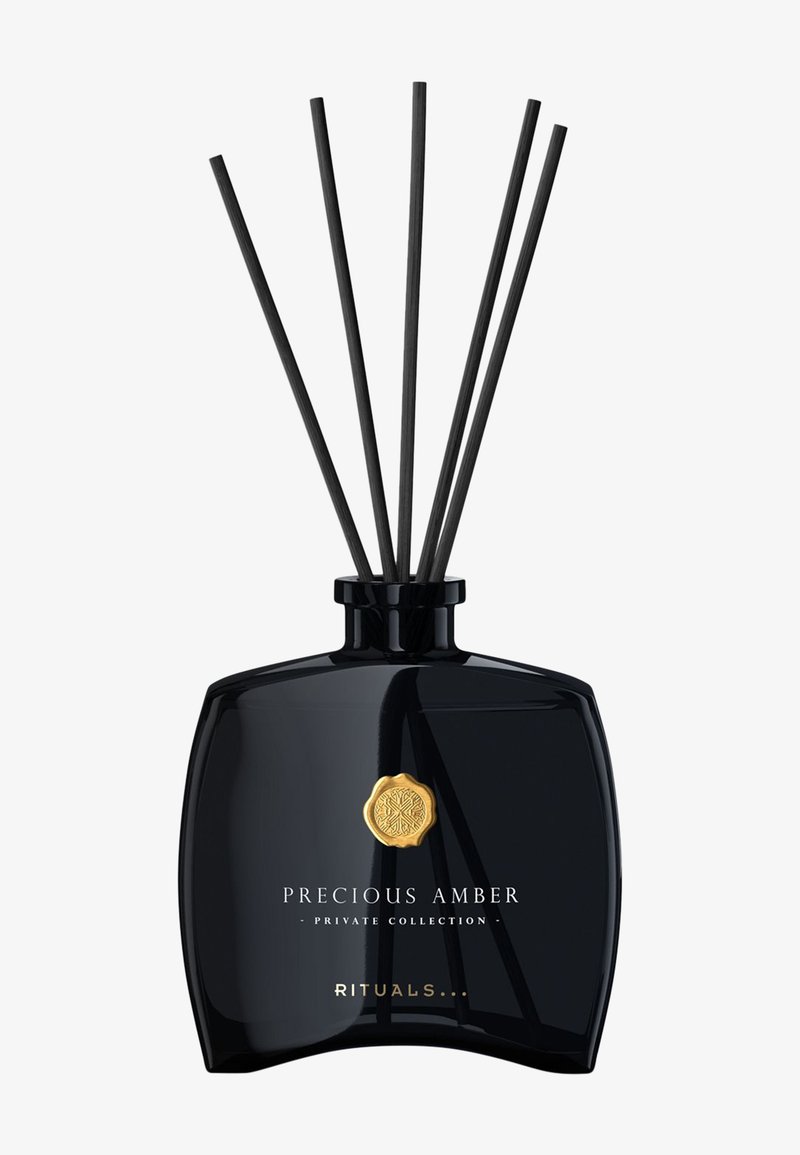 Sort glassdiffuserflaske med seks svarte rottingpinner, gull emblem, merket "Precious Amber Private Collection" av Rituals.