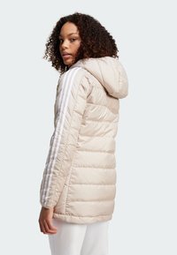 Svijetlosmeđa puffer jakna s kapuljačom, s bijelim vertikalnim prugama na rukavima, quilted teksturom i prilagođenim krojem.