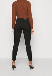 Svarta höga skinny jeans med en slät yta, tillsammans med en rostfärgad stickad tröja med ett ribbat mönster och långa ärmar.