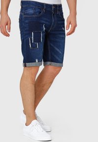 Dunkelblaue Jeansshorts mit abgenutzten Stellen, umgeschlagenen Säumen und subtilen Verfärbungen. Verfügt über ein Fünf-Taschen-Design und Gürtelschlaufen.