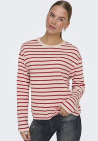 Camisa de manga larga a rayas rojas y crema con cuello redondo y corte holgado. Tejido suave con detalles de costura visibles.