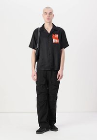Zwarte korte mouw knoopshirt met een vlamgrafiek. Draagt u met zwarte cargobroeken en zwarte sneakers. Eenvoudig ontwerp met een ontspannen pasvorm.