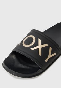 Sandales noires à glissière featuring une large bande avec l'inscription dorée "ROXY". Fabriquées en matériau synthétique avec un semel en relief et un dessus lisse.