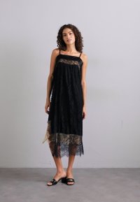 Μαύρο φορεμα με δαντέλα, με διάφανο στρώμα στο τελείωμα, διαθέτοντας τιράντες spaghetti και άνετη εφαρμογή. Υφή δαντέλας και αντίθετο γυμνό υποστρώμα.