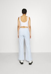 Top corto blanco con canalé y espalda baja, combinado con pantalones de pierna ancha en azul claro y botas de plataforma negras. Estilo minimalista.