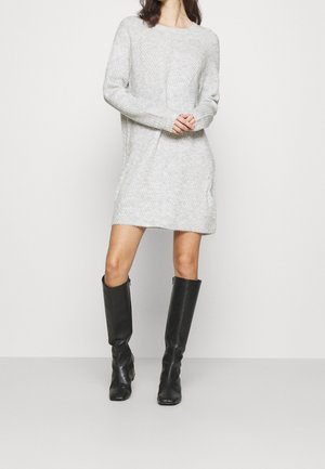 Abito maglione grigio a maniche lunghe, con texture a coste e tasche laterali. Abbinato a stivali neri in pelle alti fino al ginocchio.