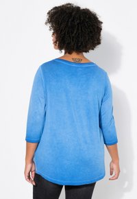 Chemise en tissu doux bleu avec des manches trois-quarts, un col rond et un effet dégradé de couleur, passant du bleu clair au bleu foncé.