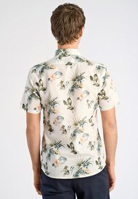 Camisa de manga corta hecha de tela ligera con un fondo crema decorado con follaje verde y patrones florales en tonos rosas. Cuello clásico y dobladillo curvo.
