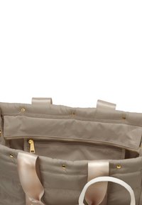 Sac beige matelassé avec quincaillerie dorée, anses en satin et une poche zippée à l'intérieur. Texture douce avec un design gonflé.