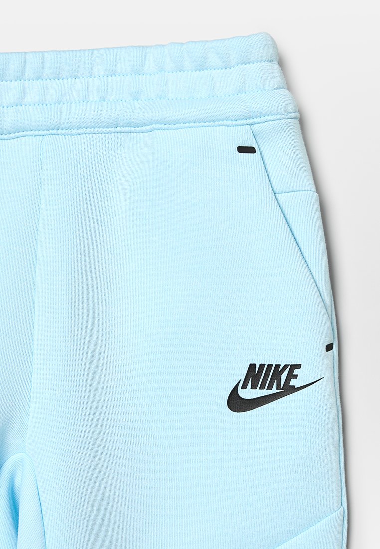 Pantalons de survêtement Nike bleu clair avec une taille élastique, des poches latérales et un logo Nike noir sur la cuisse gauche. Texture de tissu lisse et extensible.