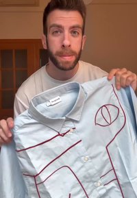 Svetlomodrá košeľa s golierom, s kontrastným červeným vyšívaným obrysom a dekoratívnym motívom oka. Zapínanie na gombíky a voľný strih.