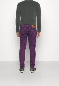 Lila jeans med en blekt textur, femfickorsdesign och en brun läderlapp på midjebandet, kombinerat med en grå långärmad tröja.