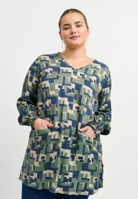 Langärmlige Tunika in einem geometrischen Muster aus Grün, Marineblau und Beige. Mit V-Ausschnitt, elastischen Manschetten und zwei vorderen Taschen. Weicher Stoff.