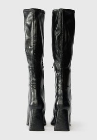 Juodos odinės iki kelių aulinės su lygiu paviršiumi, kampiniais blokuotais kulnais ir užtrauktuku gale.