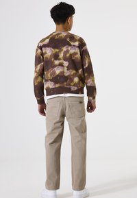 Braun-lila Batik-Sweatshirt mit langen Ärmeln, kombiniert mit hellbeigen, gerade geschnittenen Hosen und weißen Sneakers, von hinten betrachtet.